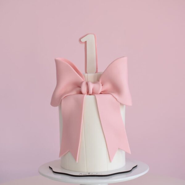 Torta cumpleaños cubierta de fondant blanca con lazo rosado